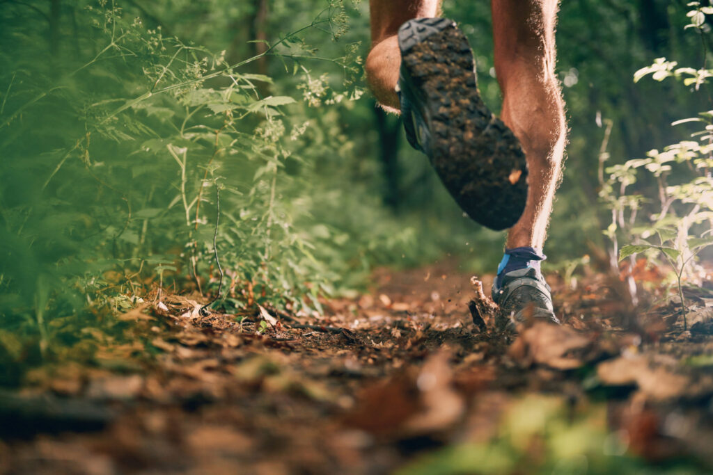 Leg detail of a competitive, athletic young man running off road outdoors through the woods on a trail in the afternoon wearing 1sportswear.