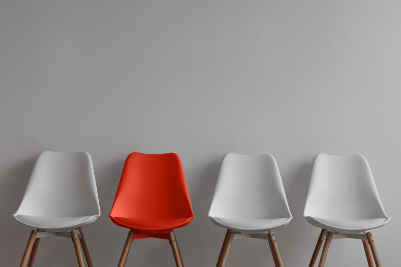 One red chair sits in the middle left of three white chairs. © By Prostock-studio/stock.adobe.com